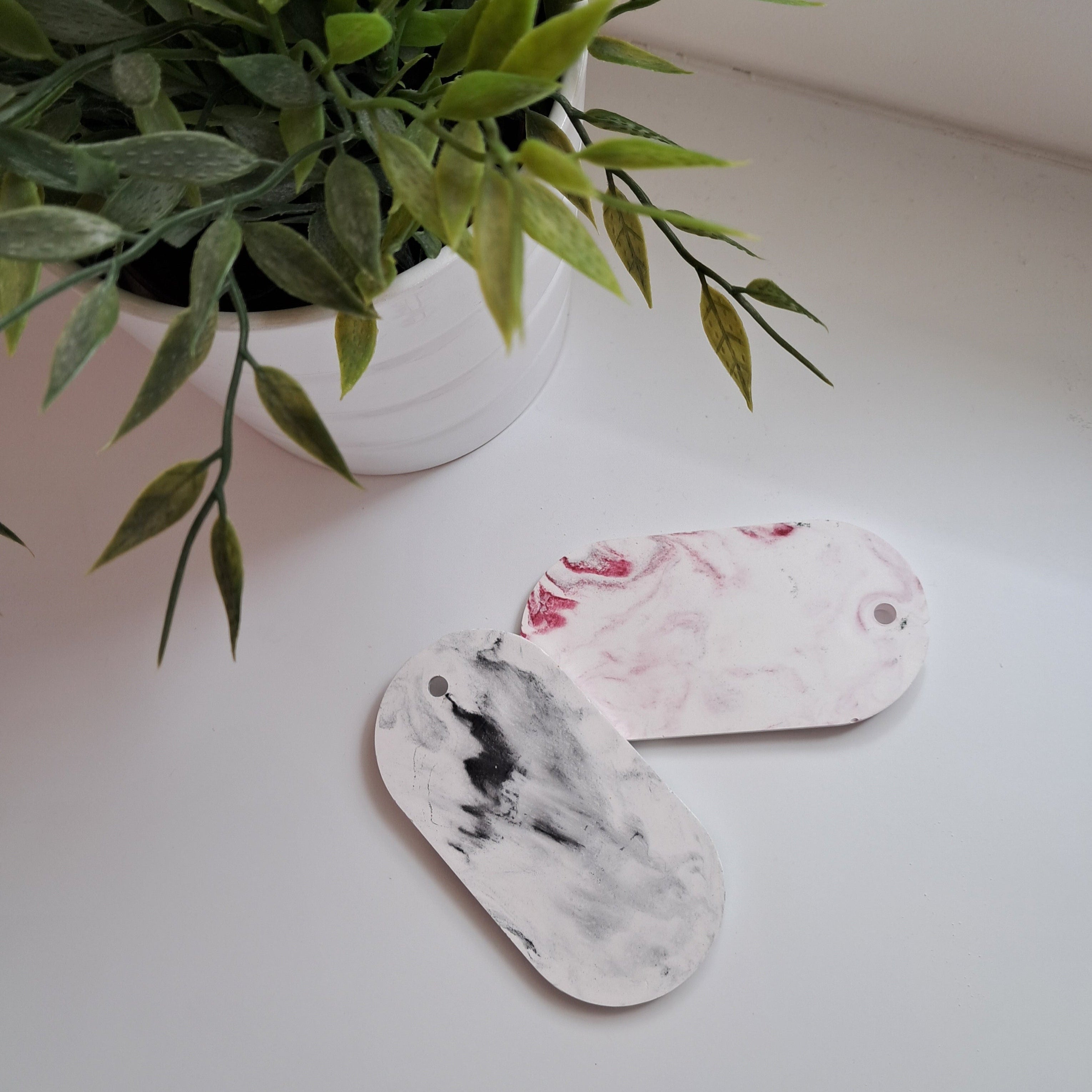 Two marble-patterned tags on a white surface with a potted plant in the background.